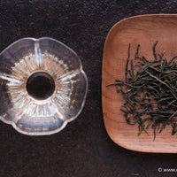 Chinese green tea Enshiyulu, steamed dry loose-leaf on wooden tray, bright transparent infusion in glass cup