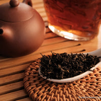 Tianjian cha dark black tea, fermented, in original bamboo leaf basket; 2014 harvest from China in glass server with Yixing teapot