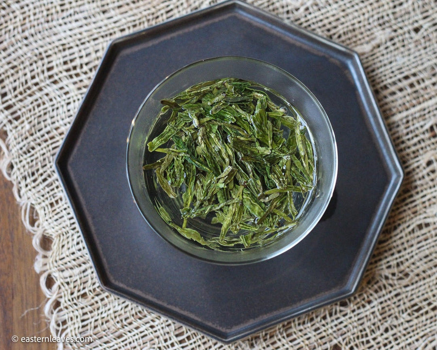 Longjing from Xihu Meijiawu, cultivar 43 Chinese green tea pre-rain, loose-leaf infused in glass gaiwan teaware on black tray from Dehua, China
