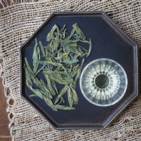 Longjing from Xihu Meijiawu, cultivar 43 Chinese green tea pre-rain, loose-leaf in glass cup on black tray from Dehua, China