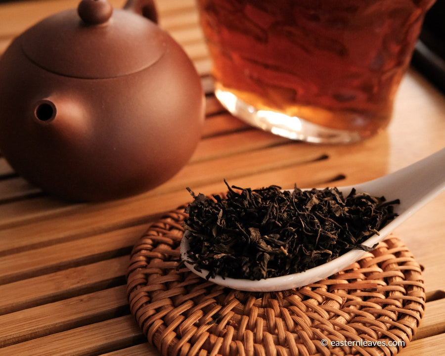 Tianjian cha dark black tea, fermented, in original bamboo leaf basket; 2014 harvest from China in glass server with Yixing teapot